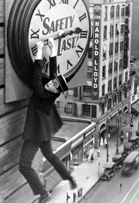 Image of Harold Lloyd clinging to hands of a clock on side of building.