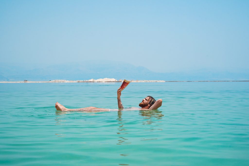 photo of a man floating in green water and reading a book