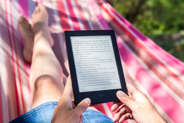 Person lying on a bright pink and red hammock holding an e-book reader